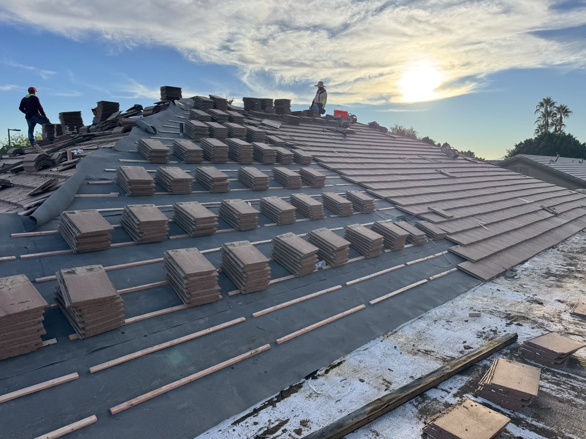 Tile roof installation in progress at golden hour, fresh tiles staged on the battens